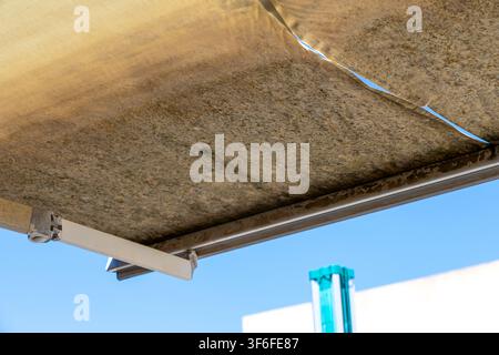 Close-up view of an aged and dirty retractable patio canopy with visible mold and damage against a clear blue sky Stock Photo