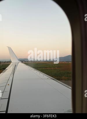 View from an airplane window with wing at sunset before takeoff, capturing travel, aviation and summer journey atmosphere. Stock Photo