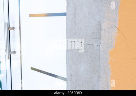 A detailed view shows hairline fractures on a rough concrete surface adjacent to a sleek, contemporary glass entrance with metal accents Stock Photo