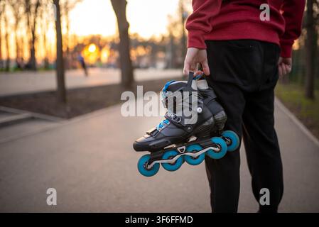 Close up of a person holding a pair of black inline skates at sunset Stock Photo