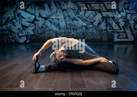 Bearded breakdancer in baseball cap doing wide leg stretch Stock Photo
