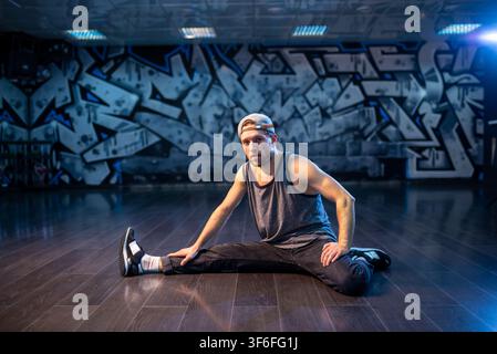 Bearded breakdancer in baseball cap doing wide leg stretch Stock Photo