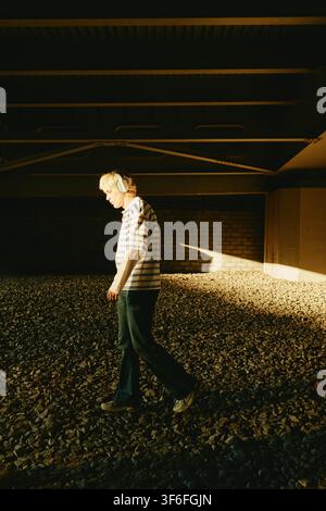 Man Wearing Headphones Walking Outdoors under Bridge Stock Photo