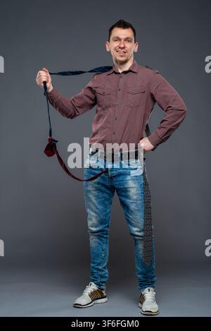 Smiling man in a brown shirt holding a long tie out from his jeans zipper Stock Photo