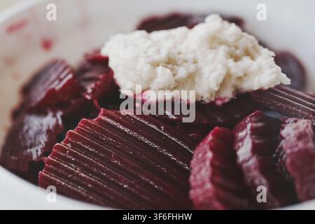 Close-up of fresh sliced boiled beetroot salad topped with spicy white grated horseradish in a ceramic bowl. Stock Photo