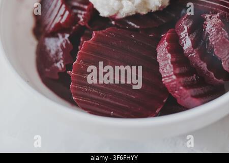 A close-up shot of sliced pickled beetroot salad served with grated white horseradish in a white bowl, capturing the vibrant red texture and rich culi Stock Photo