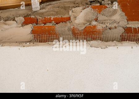 Detail of a building facade under construction, showing exposed brickwork, reinforcing mesh, and wet plaster being applied Stock Photo