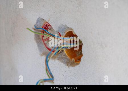 Close-up view of frayed electrical wires with various colors protruding from a broken wall cavity, suggesting unfinished construction or repair Stock Photo