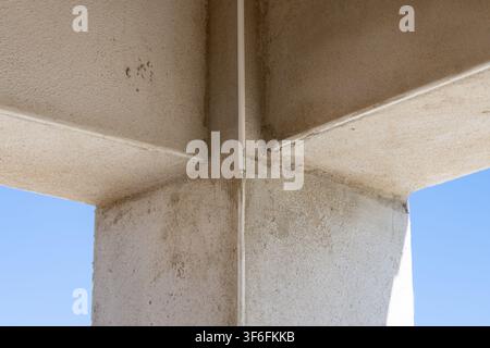 The textured surface of a structural concrete column meets at a sharp angle, with a thin white pipe running vertically along the seam Stock Photo