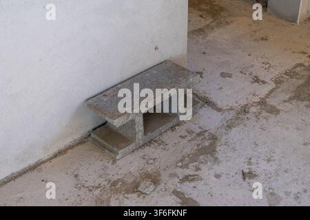 A single gray cinder block sits on a dusty concrete floor beside a rough, unfinished wall in a construction setting Stock Photo