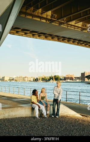 Diverse People Hanging out by River under Bridge Stock Photo