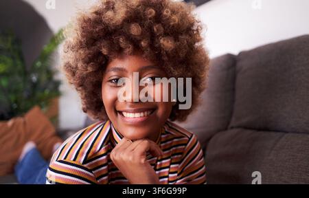 Cheerful portrait of an African young woman looking at camera smiling while lying at home at night. Stock Photo