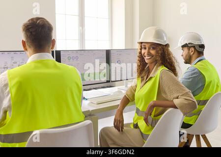 Female engineer in hard hat monitoring industrial dashboards in control room Stock Photo