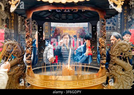 New Taipei City, Taiwan - Feb 17, 2026: Worshipper inserting incense into golden censer at Luzhou Baohe Temple, symmetrical close-up, devout scene Stock Photo