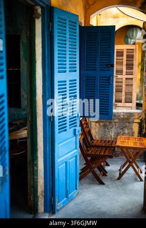 Vintage blue colored wooden doors and table with chairs setting in traditional cafe in Hoi An. Stock Photo