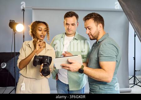 Photographers Team Reviewing Images on Tablet in Studio, Planning Lighting Setup Stock Photo