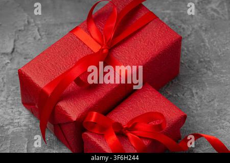 Two red gift boxes wrapped in textured paper with satin ribbons and bows on a grey concrete background, holiday celebration concept. Stock Photo
