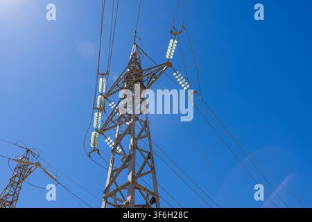 Close-up view of electrical pylons and overhead cables carrying energy across the landscape under a bright sunny day Stock Photo
