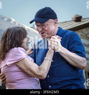 An elderly couple dance and laugh together at an outdoor park concert. Stock Photo