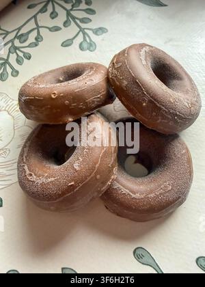 Four frozen chocolate ring doughnuts stacked on a floral tablecloth, viewed from above Stock Photo