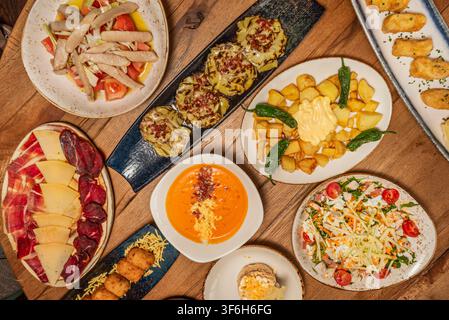 Overhead spread of Spanish tapas: cured meats, salmorejo, patatas bravas, croquettes, salad and grilled artichokes on wooden table Stock Photo