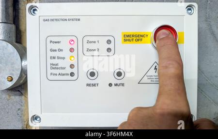 Engineer operating an emergency shut off button on an industrial gas detection control panel in a commercial plant room. Safety equipment used to isol Stock Photo