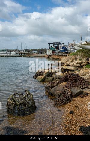 Old lobster pot and rusty chains on the shoreline next to an old boatyard in Bembridge harbour on the isle of wight, UK Stock Photo