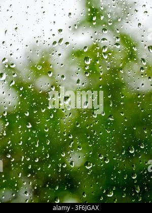 Espoo, Finland - 12.06.2017: Close-up of water droplets on a transparent pane against a soft bokeh of vibrant green trees Stock Photo