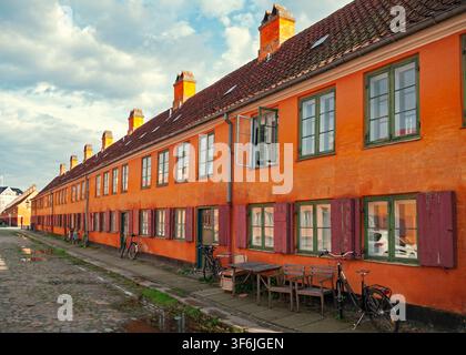 Copenhagen, Denmark - 30.07.2017: Row of traditional terracotta-colored naval barracks in Nyboder featuring red shutters and cobblestone road Stock Photo
