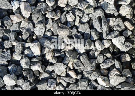 Top-down close-up of angular gray crushed stone gravel, showing a dense mix of sharp-edged rock fragments in varying shades of gray, black, and white. Stock Photo