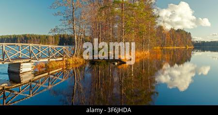 Kyynärä, Finland - 21.10.2017: Rustic timber pier and autumn foliage on a small island mirrored in a still lake with fluffy white clouds Stock Photo