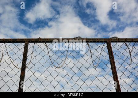 Background of wire mesh fence with rusty barbed wire under the blue sky Stock Photo