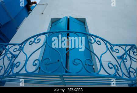 Burano, Italy - June 20, 2026: Low angle architectural detail of a white plaster facade featuring bright blue wooden window shutters and an ornate met Stock Photo