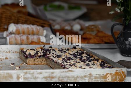 Baked dessert featuring berry filling and crumb topping in a white tray, with assorted pastries and a small floral arrangement on a rustic wooden tabl Stock Photo