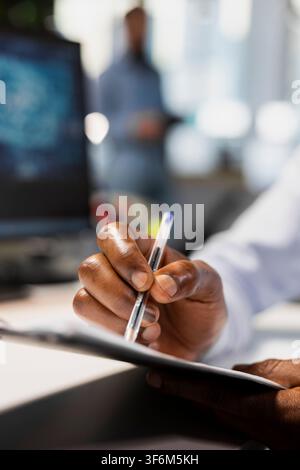 Close up of office employee filling out paperwork on clipboard at desk helped by AI software. Worker manages documentation tasks using artificial intelligence tools for support and accuracy Stock Photo