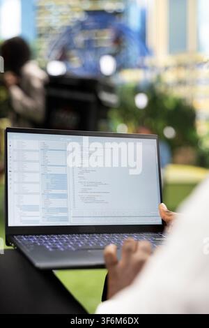 Close up of person working with programming interface and source code on laptop, representing software development and flexible IT work in city park. Over-the-shoulder view. Stock Photo