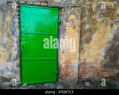 Vibrant green metal door set in an old rustic brick and plaster wall. Stock Photo