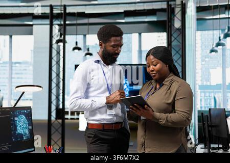 Teamworking engineers in office using AI on device to streamline app development. IT colleagues using tablet to run debugging applications with machine learning technology Stock Photo