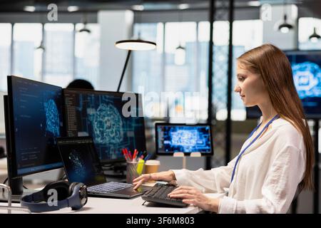 Young system administrator in office relies on AI tech to run tasks across multiple devices, monitoring progress on screens. Tech company intern uses neural networks to develop artificial intelligence Stock Photo