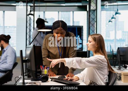 Joyous supervisor pleased by code snippets written by junior dev in modern workspace, adjusting configurations. Team leader satisfied with work dove by intern monitoring API cloud services Stock Photo