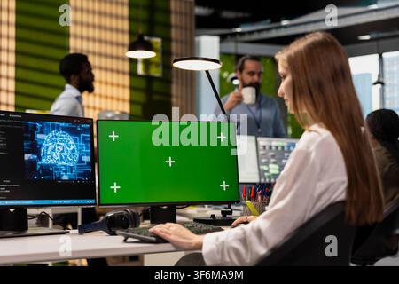 Junior dev in tech startup uses AI on green screen PC to optimize performance and forecast issues. Young female engineer writing code in office, training machine learning models using mockup computer Stock Photo