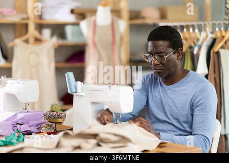 Working in sewing workshop - male tailor working at sewing machine making stitches on fabric Stock Photo