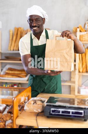 Male baker holding a brown paper bag in a bakery Stock Photo