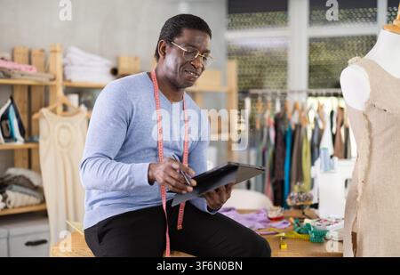 Male tailor draws sketch of future clothing on an electronic tablet. Working with modern gadgets in sewing workshop Stock Photo