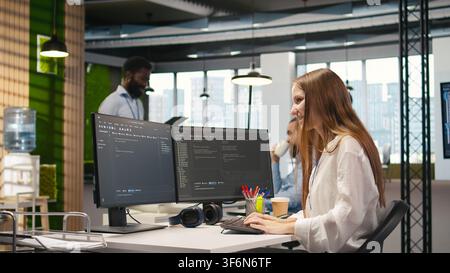 Young female programmer using computer to write code, developing machine learning APIs. Junior developer troubleshooting software errors and faults using artificial intelligence, camera A Stock Photo