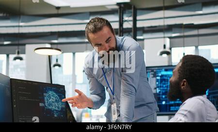 Startup engineer and colleague with paraplegia brainstorming, working with machine learning tech. Man in wheelchair and coworker in office transforming data into AI predictive models, camera A Stock Photo