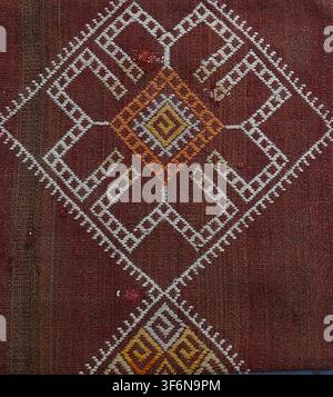 Hand-woven moroccan kilim rug presenting a close-up view of its coarse red fabric textured background, intricate white, orange, and yellow geometric p Stock Photo