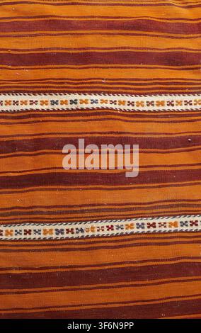 Handwoven kilim rug with earthy orange and brown horizontal stripes, accented by white bands and colorful geometric embroidery, showcasing traditional Stock Photo