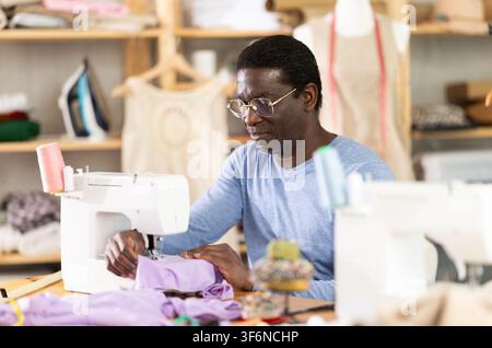African American man tailor sews clothes in sewing machine. Stock Photo