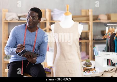 Experienced tailor designing custom dress using tablet in studio Stock Photo